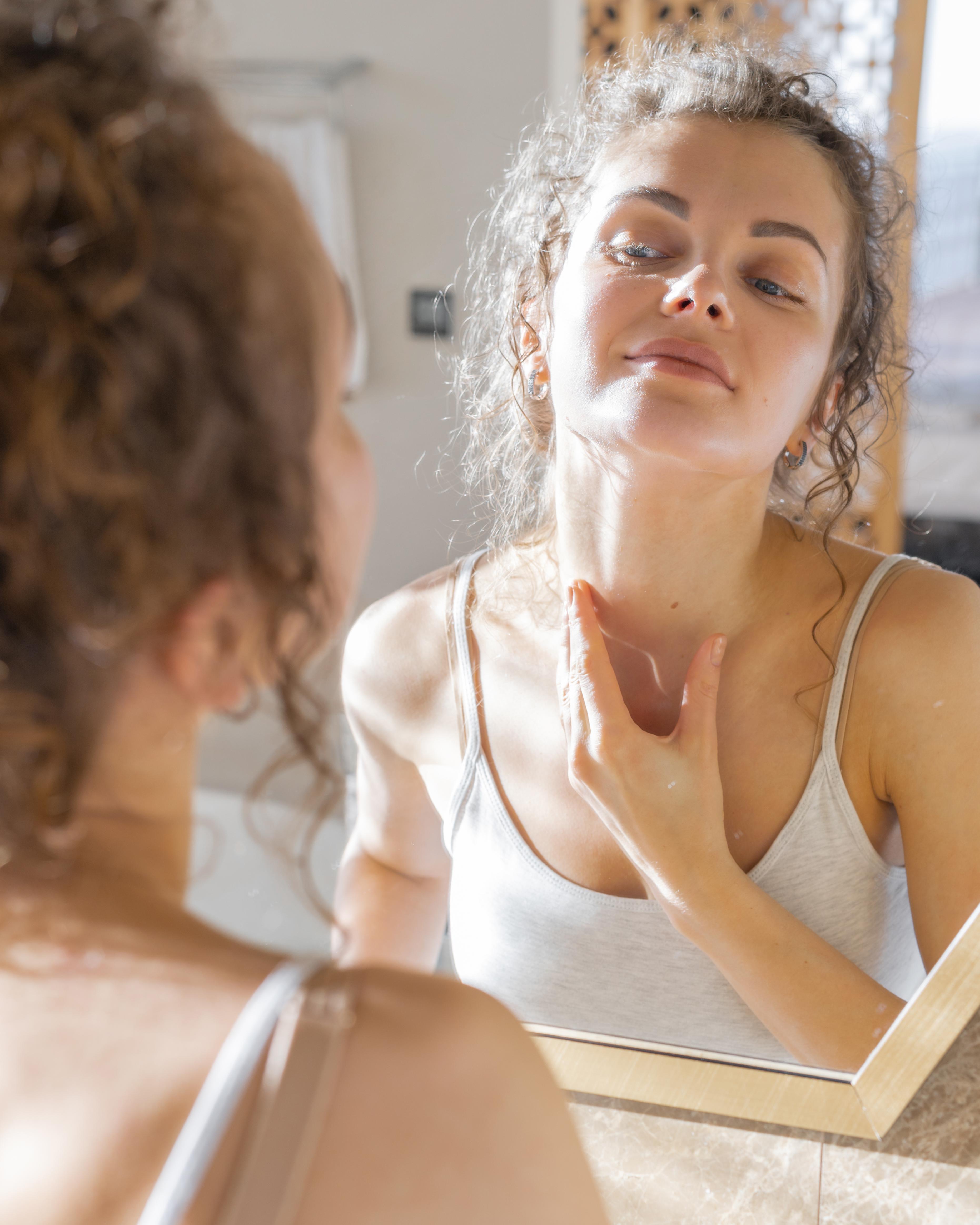 woman-looking-mirror-applying-cream-neck